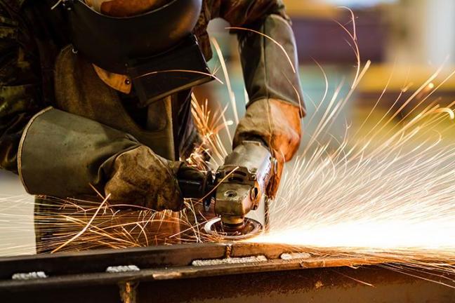 Industrial worker grinding metal with sparks flying